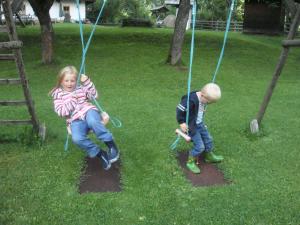 two children playing on a swing in a yard at Ferienwohnung Lahnerhof in Arriach