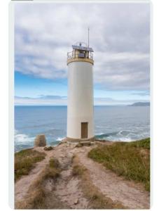 a lighthouse on top of a hill near the ocean at Vivienda Turística Ático in Laxe