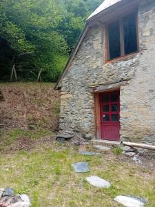 a stone house with a red door in a field at Cabane du Serris - Expérience insolite dans les Pyrénées in Beaudéan +5 photos