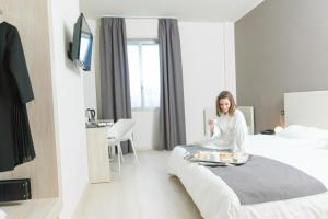 une femme assise sur un lit dans une chambre d'hôtel dans l'établissement Helios Hotel & Restaurant, à Monza