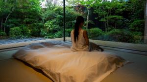 a woman sitting on a bed looking out a window at Comico Art House Yufuin in Yufu