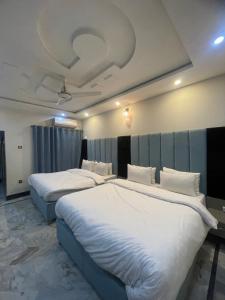 two beds in a hotel room with white sheets at Aban Guest House in Peshawar
