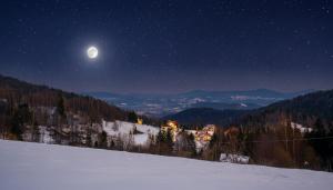 a full moon rising over a snowy mountain at night at Noce pod Gwiazdami in Sidzina
