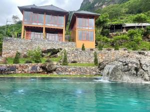 a house with a waterfall in front of a body of water at HagiangHillside in Ha Giang