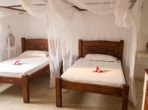 two beds in a room with white sheets and flowers on them at Spacious accessible house in Watamu, shared pool in Watamu