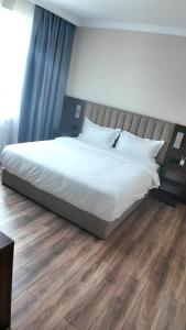 a bed with white sheets and pillows on a wooden floor at Elegance Hotel Osh in Osh +7 photos