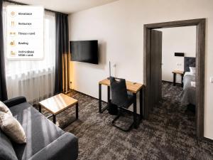 a living room with a couch and a desk in a hotel room at Olympland Hotel in Trutnov