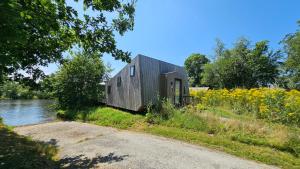 a small black house sitting on the side of a river at Tiny House De Klyster in Westergeest