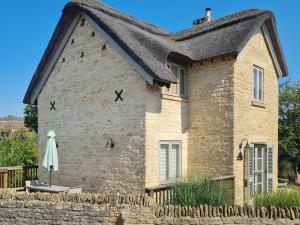 a stone house with a black roof and an umbrella at Moorhens Cottage in Somerford Keynes