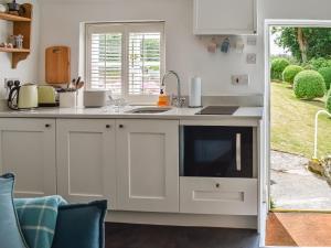a kitchen with white cabinets and a sink and a window at Tan Bryn - Uk44151 in Llanallgo