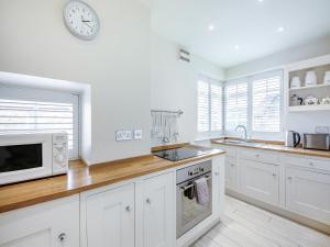 a kitchen with white cabinets and a clock on the wall at Chareside Cottage in Corbridge +12 photos