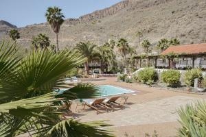 a resort with a pool and palm trees and a mountain at Finca rural Los Tanquillos in San Bartolomé