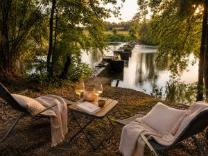 a table and chairs next to a river with wine glasses at THOUARS Rivière LODGE KAËLI in Maulais