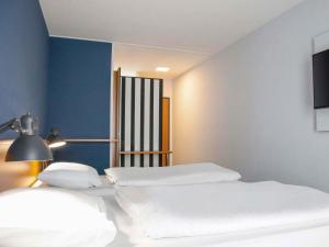a bedroom with two beds and a lamp and a chair at B&B HOTEL Dresden-Altstadt in Dresden