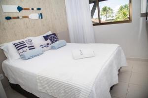 a white bed with blue and white pillows on it at Flat Resort Beira Mar Porto de Galinhas in Ipojuca +51 photos