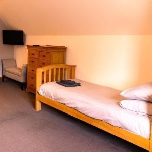 a bedroom with a wooden bed with a dresser and a chair at Ardbrae Cottage in Daviot