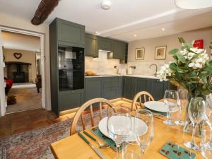 a kitchen with green cabinets and a wooden table with wine glasses at Little Wickers in Wareham