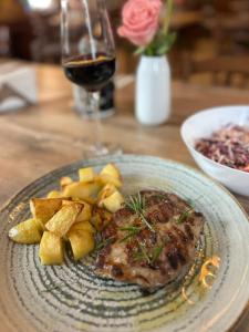 a plate of meat and potatoes with a glass of wine at Bran Pensiunea Restaurant Al Gallo centru in Bran