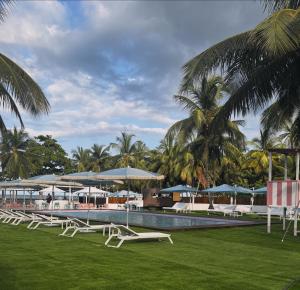 a pool with white chairs and umbrellas and palm trees at Roulotte Beach São Tomé in Triunfo