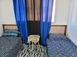 two beds in a room with blue curtains at Aïn turk oran in Aïn El Turk