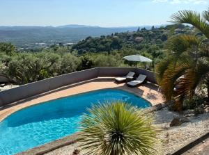 a swimming pool with two chairs and an umbrella at Évasion au calme in Montauroux
