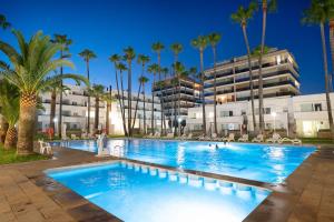 a large swimming pool with palm trees in front of a building at Apartamentos Tamarindos Peñiscola in Peniscola