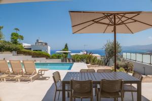 a table with chairs and an umbrella next to a swimming pool at Esprit Villas in Polis Chrysochous