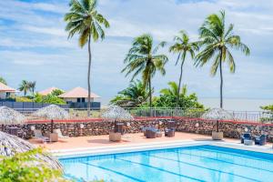 a swimming pool with chairs and palm trees at Hotel des Roches in Kourou