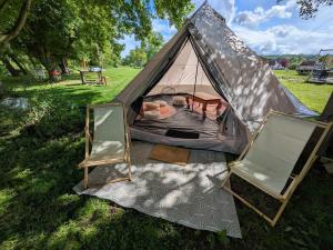 a tent with two chairs and a table in a field at Quiet Riverside Apartment in Grosley-sur-Risle