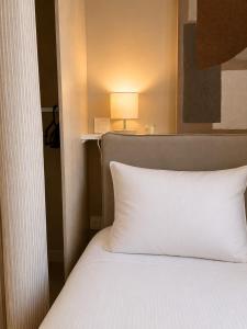 a white bed with a white pillow and a lamp at Le Mas d'Elio in Cheval-Blanc