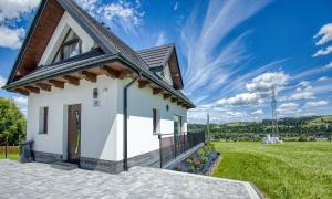a white house with a balcony and a grassy field at Mery House Agroturystyka in Biały Dunajec