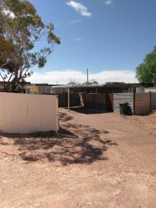 a dirt yard with a fence and a tree at Cave Place Units in Coober Pedy