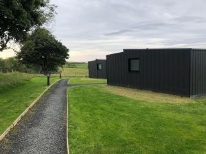 a black house on a gravel road next to a field at Luxury Glamping Cabin sleeping 4 People with Private Hot Tub and BBQ with views across the North Coast Ballycastle Pod 2 in Ballycastle