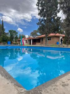 a blue swimming pool with a house in the background at Cabañas Splash Valladolid in Jesús María