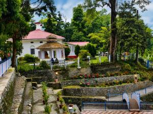a white building with a pink roof and a garden at Ningma Lamu Homestay in Mangpu