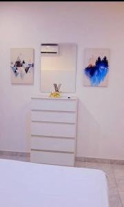 a white bedroom with a dresser and paintings on the wall at takara stay in Delmas