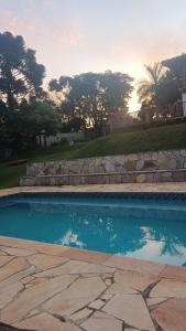 a swimming pool with a stone wall and the sunset at Cura e Conexões in Jarinu