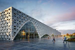 a large building with a geometric facade with people walking in front at appartement 3 gare tgv in Kenitra