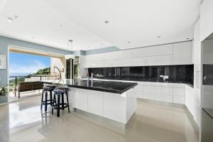 a kitchen with white cabinets and black counter stools at Villa Mariposa in Coolum Beach