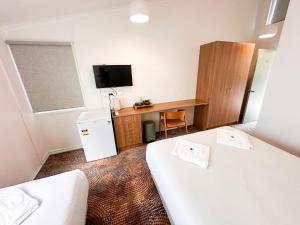 a room with two beds and a desk and a television at Bateau Bay Hotel in Bateau Bay