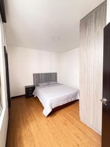 a white bedroom with a bed and a wooden floor at La Posada del Colibrí in Cuenca