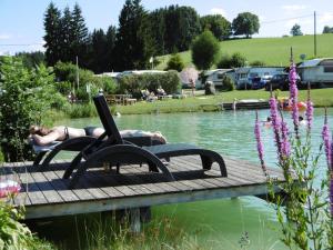 a woman laying on a bench with a laptop on a dock at Terrassen-Camping am Richterbichl in Rottenbuch