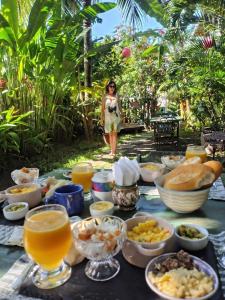 a table with food and drinks and a woman in the background at Jardim UIXA in Ilha de Boipeba