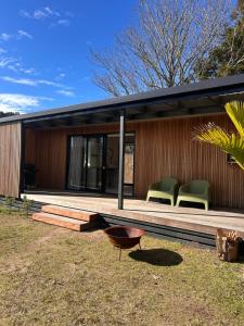 a house with green chairs on a wooden deck at Cooks Beach Studio Escape in Cooks Beach