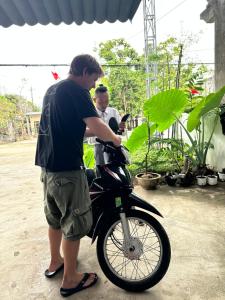 a man looking at his cell phone while standing next to a motorcycle at Captain's Home Phong Nha in Phong Nha