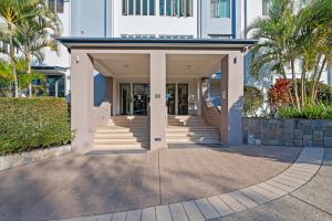 a large white building with stairs and palm trees at Moana Condo | Close to Beach in Caloundra