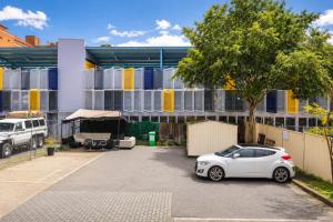 a white car parked in a parking lot in front of a building at Perth City Backpackers Hostel - note - Valid passport required to check in in Perth