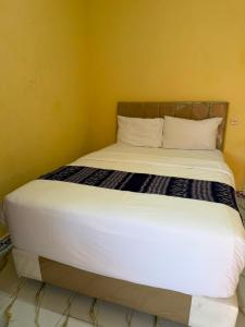 a bed with white sheets and pillows in a room at Amita Homestay in Tambolaka Airport