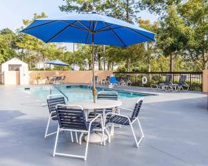 a table and chairs with a blue umbrella next to a pool at Quality Inn At the Mall - Valdosta in Valdosta