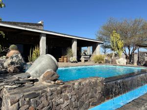 a man sitting next to a swimming pool in front of a house at 3 ALOES GUESTHOUSE in Uis